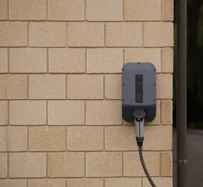 A grey home EV charger mounted on a buff brick wall.