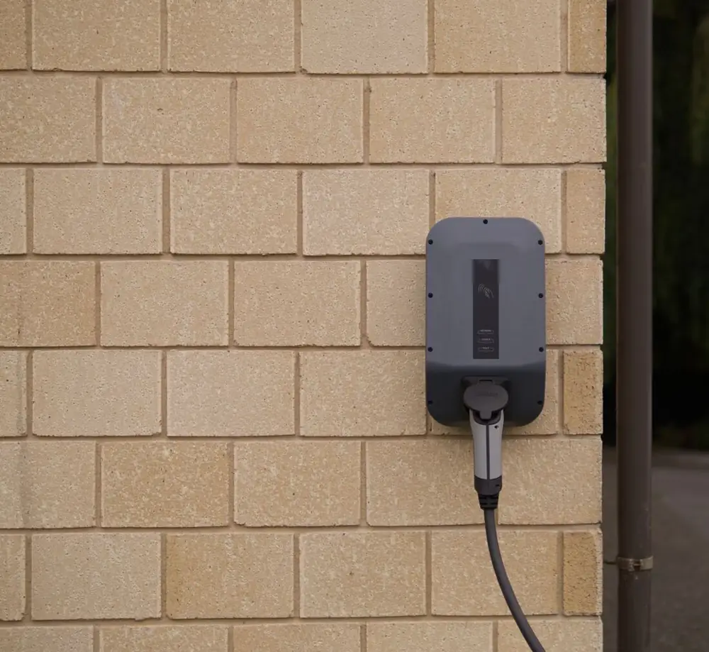 A grey home EV charger mounted on a buff brick wall.