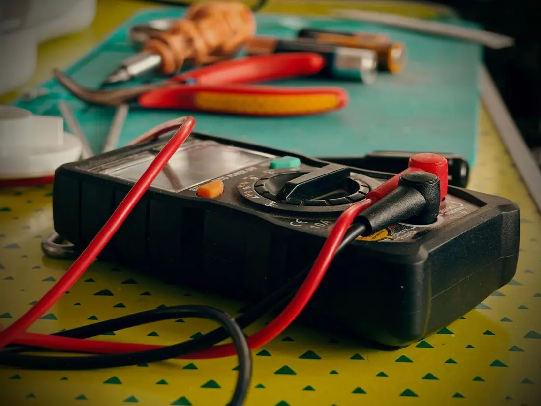 A multimeter and hand tools laid out on a workbench.