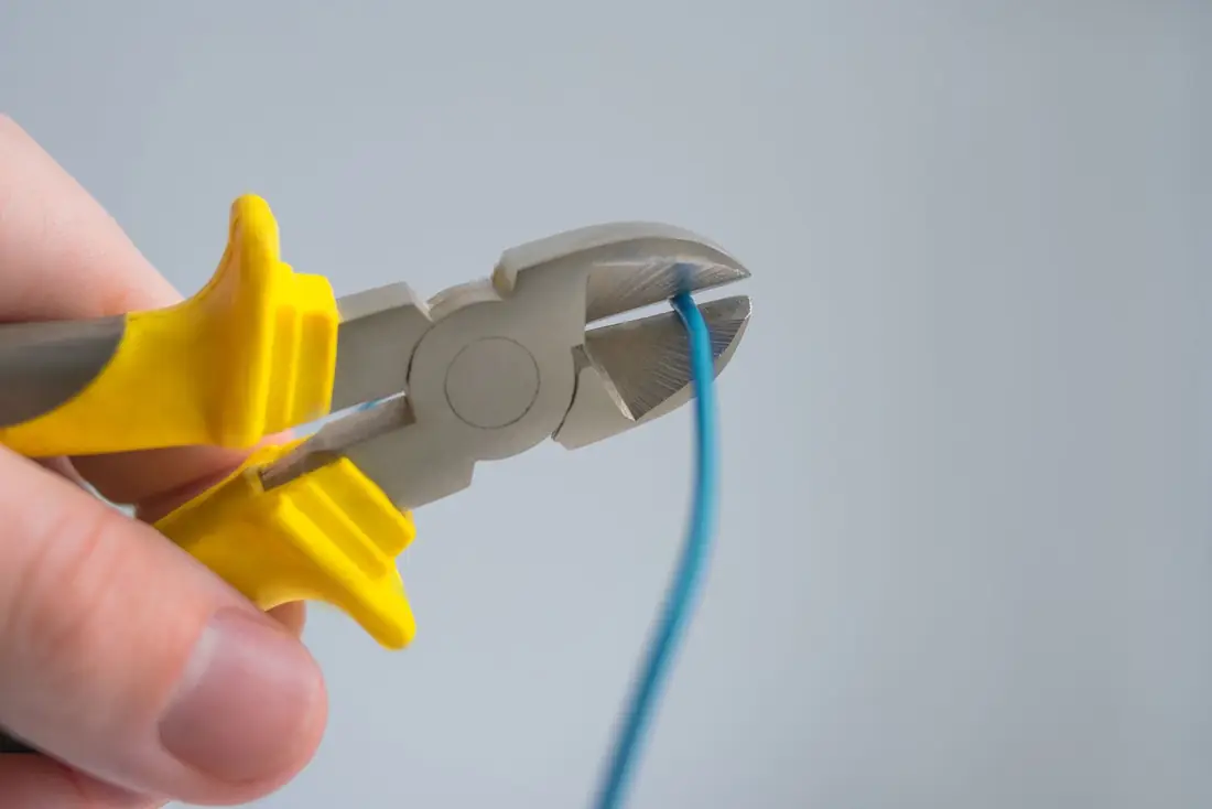A hand cutting a blue wire with yellow-handled side cutters.